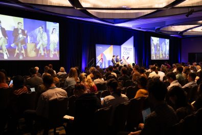 Image of crowd listening to presentation with four people on stage.