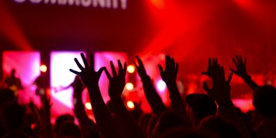 Hands raised at a concert with the word "community" in the background.