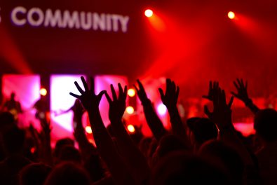 Hands raised at a concert with the word "community" in the background.